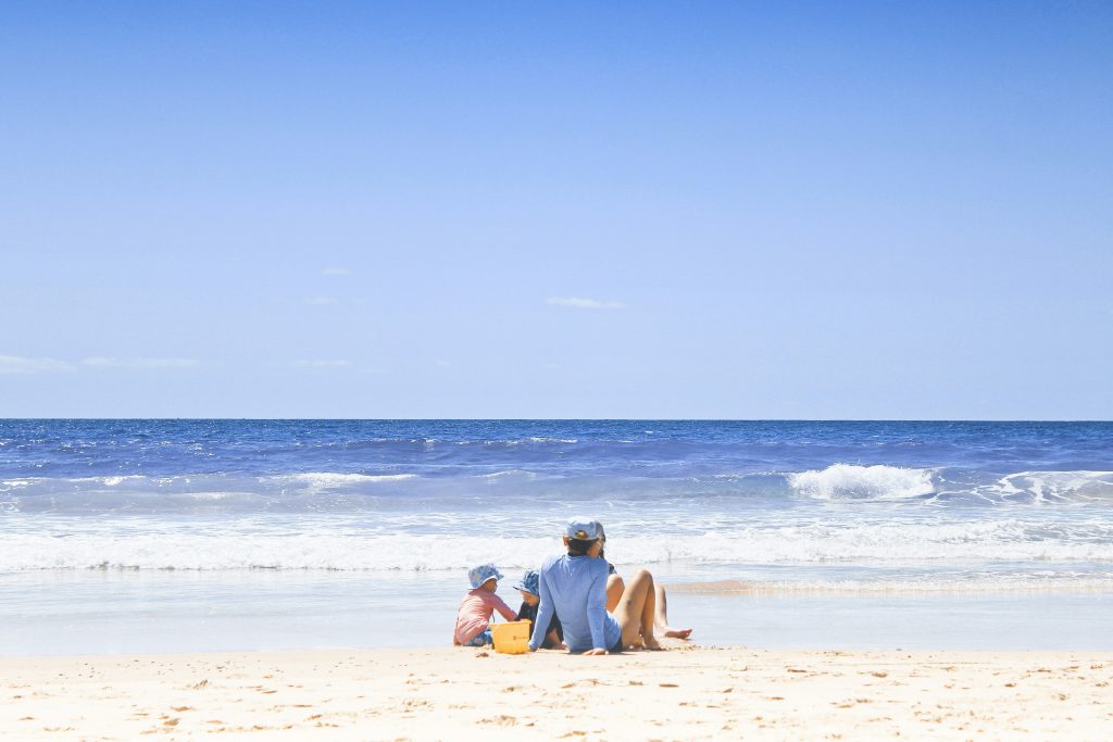 A family seated together on a sunlit beach, looking out to sea — a symbol of the lasting security that thoughtful wealth preservation and legacy planning can provide.